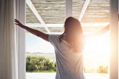 朝日を浴びながら窓辺で深呼吸する女性の後ろ姿