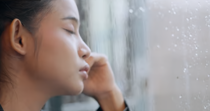 雨の窓を見ながら感じにくい悩みを考える女性