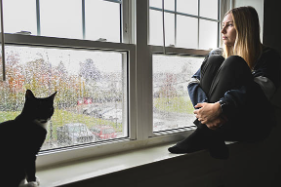 雨の窓を見ながら自分の体について考える女性