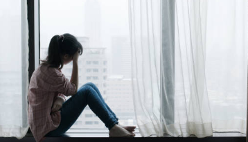 雨の窓際で自分の体について悩んでいる女性