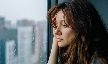 雨の窓を見ながら感じにくいことについて考える女性