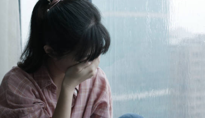 雨の窓際で自分の体の反応について悩む女性